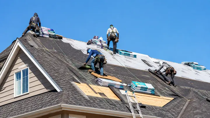 Roofing crew replacing asphalt shingles on a residential house under a clear sky