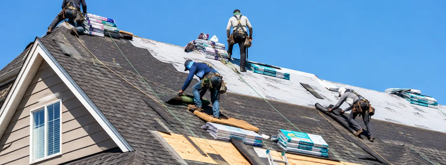 Roofing crew replacing asphalt shingles on a residential house under a clear sky