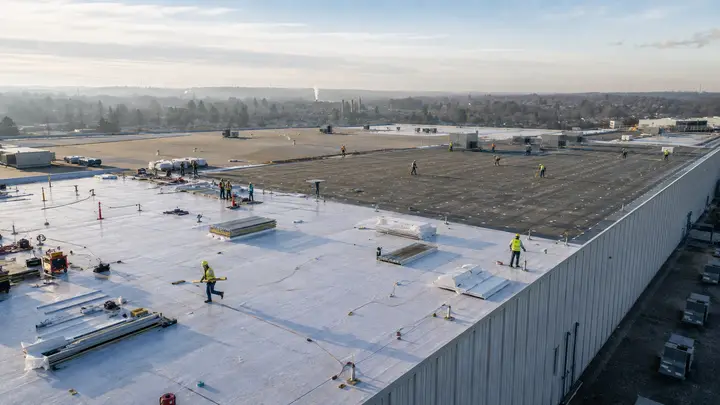 Roofing crews replacing the large low-slope roof of an industrial warehouse